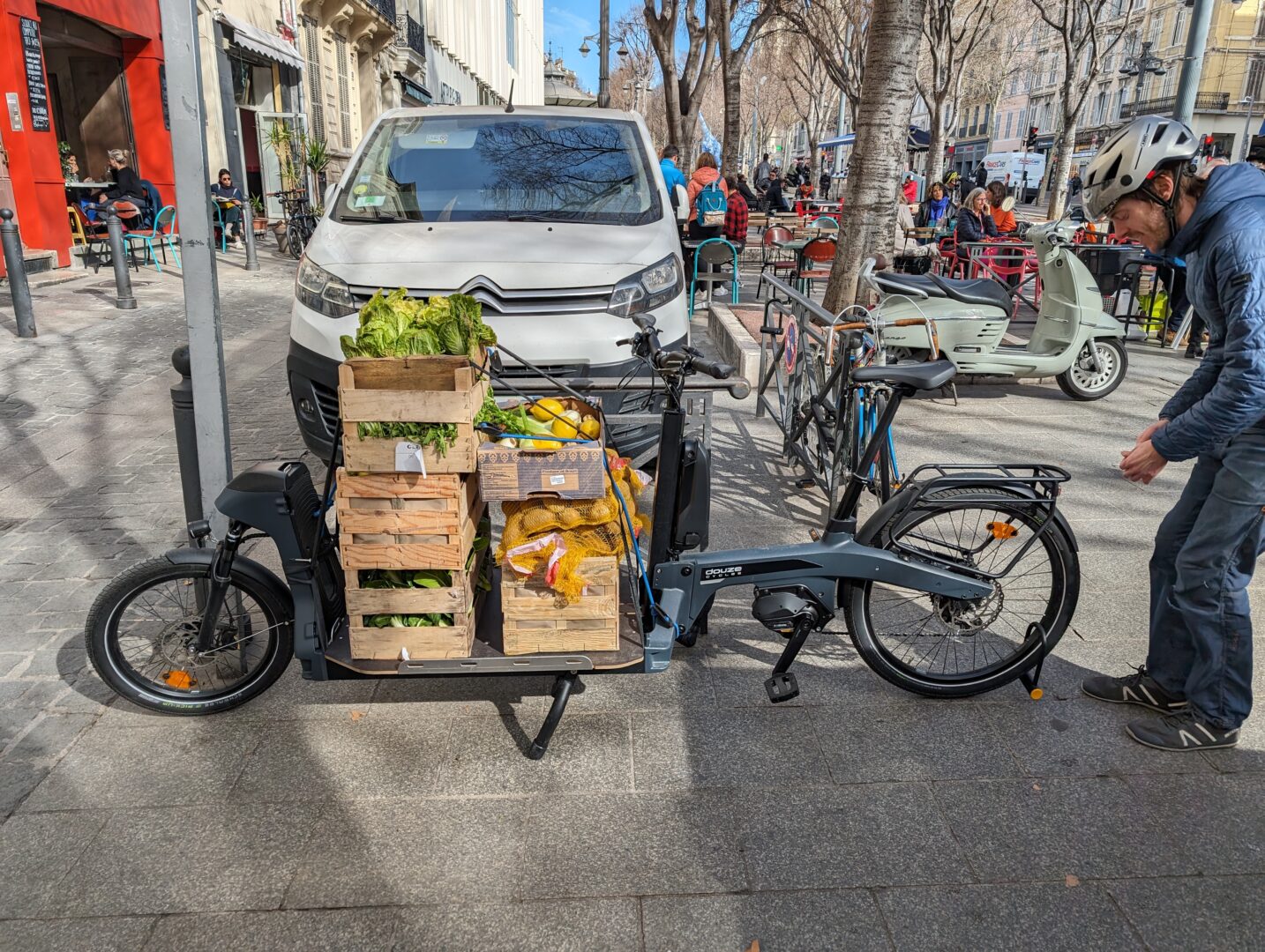 Coursier des Coursiers Solidaires récupérant des légumes frais et les transportant à vélo, favorisant la mobilité locale et l’aide alimentaire à Marseille.