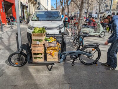 Coursier des Coursiers Solidaires récupérant des légumes frais et les transportant à vélo, favorisant la mobilité locale et l’aide alimentaire à Marseille.